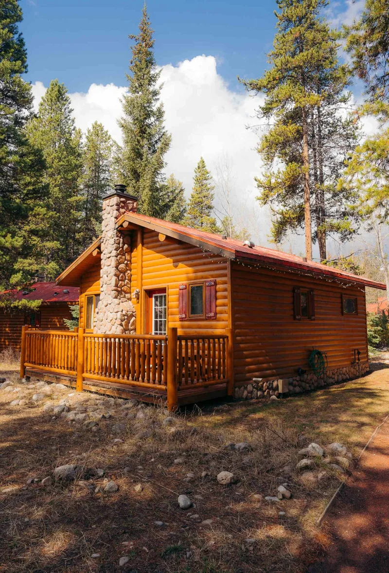 Log cabin at Baker Creek By Basecamp with timber exterior, metal roof, wooden porch, surrounded by coniferous forest.