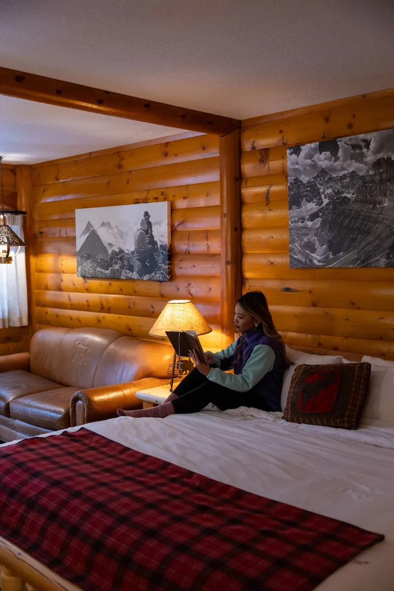 Baker Creek By Basecamp cabin interior with log walls, bed with plaid blanket, and mountain photography.