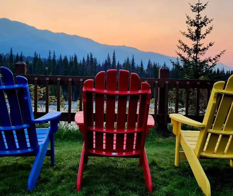 Colorful Adirondack chairs on a Becker's Chalets deck overlook forested mountains at sunset.