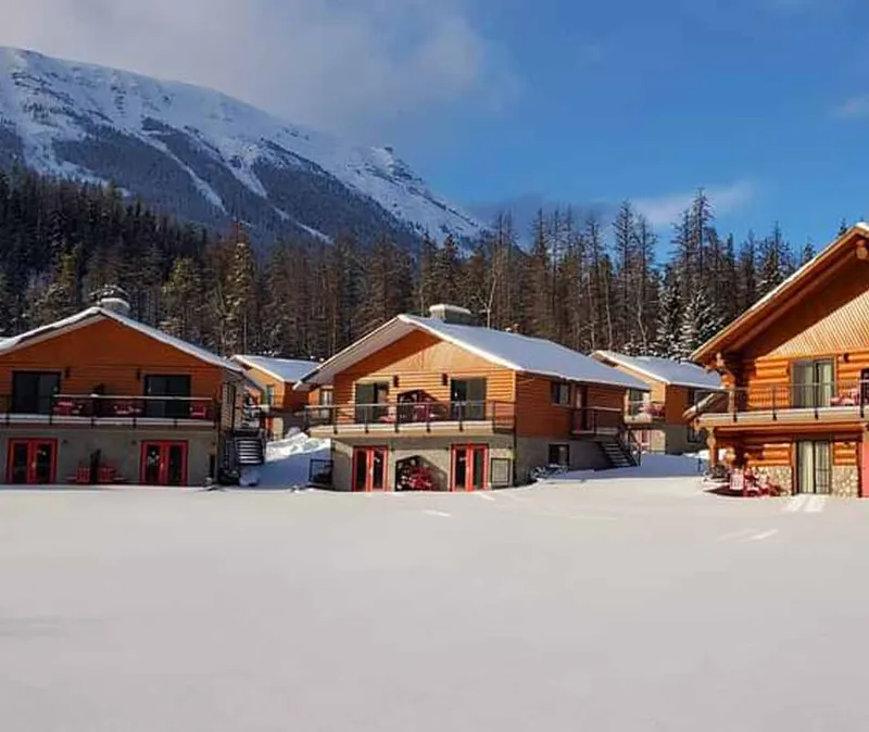 Log cabin chalets at Becker's with snow-covered peaks and forest backdrop in winter.