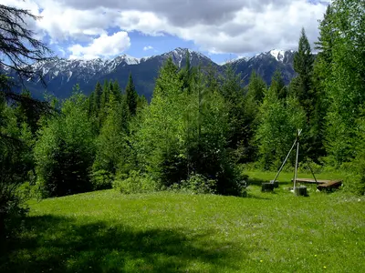 Cross River Wilderness Centre meadow with snow-capped mountains and evergreen forest backdrop.