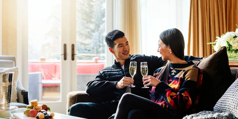 Couple toasting champagne in a Fairmont Jasper room with mountain views and fireplace.