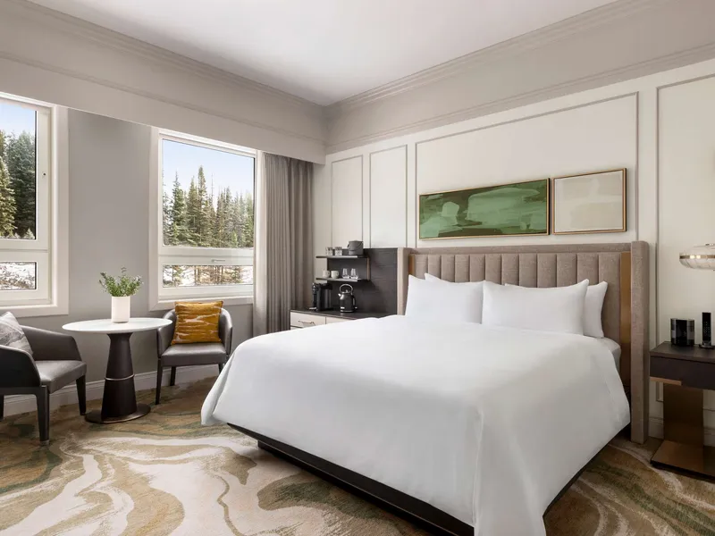 Fairmont Chateau Lake Louise guestroom with bed, seating area, and forest views from windows.