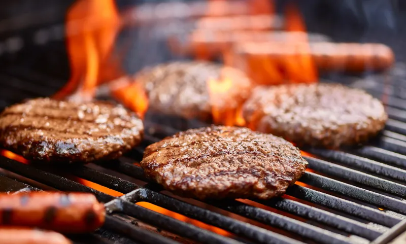 Burgers and sausages sizzling over flames on a gas grill at Hidden Ridge Resort.