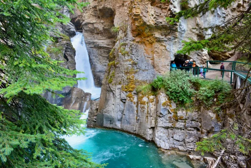 Vintage car parked at Johnston Canyon Lodge overlook above turquoise canyon waterfall and cliffs.