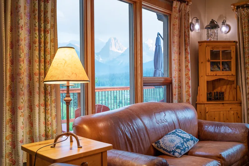 Mount Engadine Lodge interior with leather sofa, alpine peak view, and mountain lake beyond large windows.