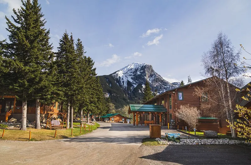 Overlander Lodge's log cabin structures with turquoise trim set against a snow-capped mountain in Jasper.
