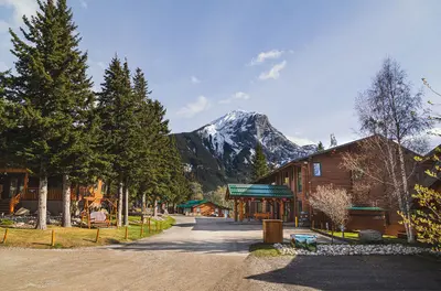 Overlander Lodge's log cabin structures with turquoise trim set against a snow-capped mountain in Jasper.