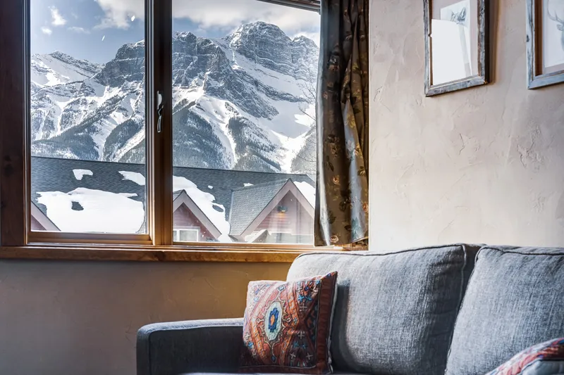 Paintbox Lodge suite with gray sofa facing snow-covered Kananaskis mountain peaks through large windows.