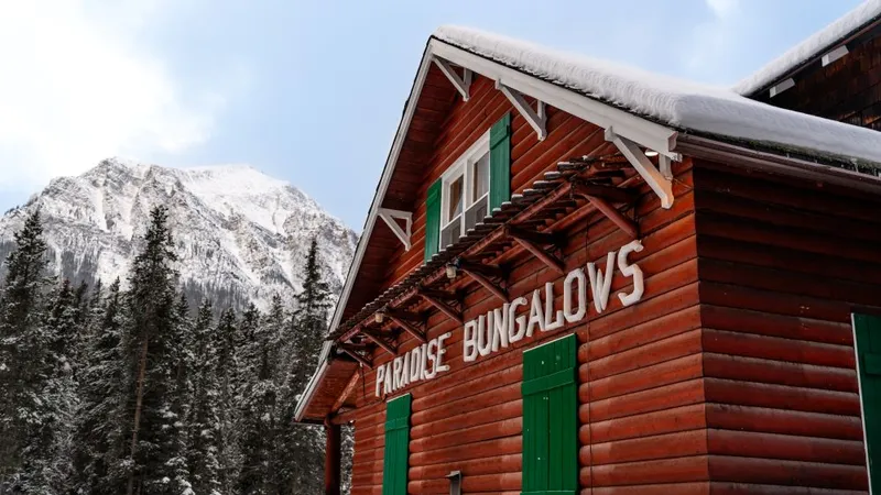 Red log bungalow with green doors at Paradise Lodge, snow-capped mountain and evergreens behind.
