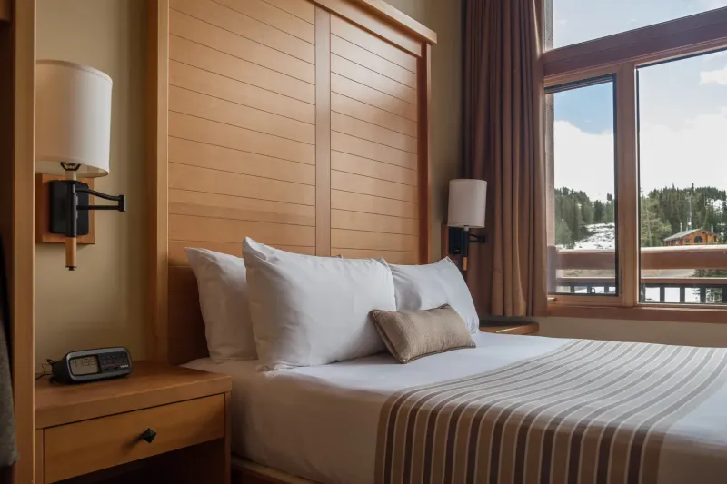 Sunshine Mountain Lodge deluxe room with wood headboard, mountain and forest views through glass doors.