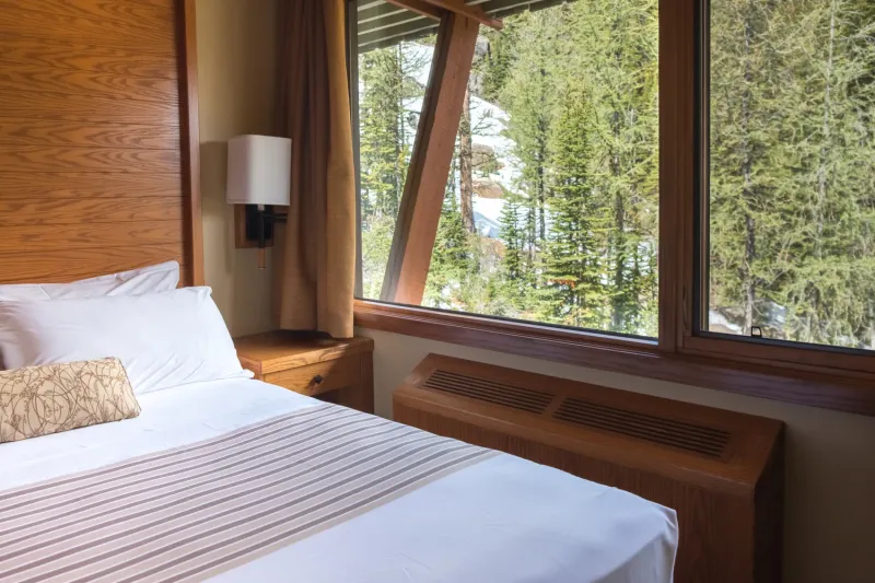 Sunshine Mountain Lodge bedroom with timber-framed window overlooking coniferous forest.