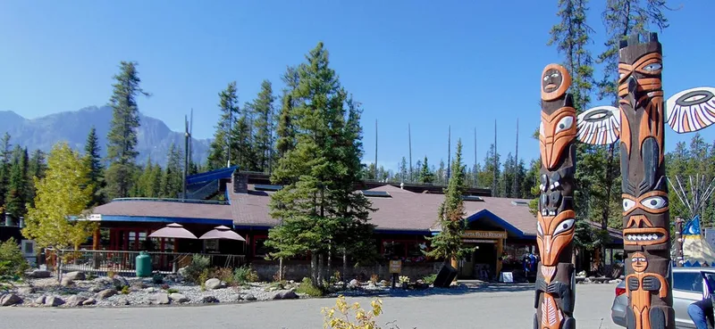 Sunwapta Falls Rocky Mountain Lodge day lodge with blue roof, timber exterior, Indigenous totem poles, and mountain backdrop.