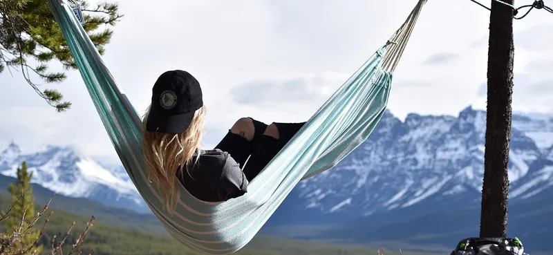 Person relaxing in hammock with snow-capped Rocky Mountain peaks behind Sunwapta Falls Lodge.