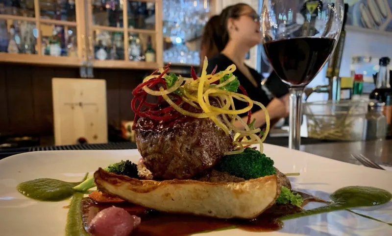 Plated steak with garnish at Sunwapta Falls Lodge's dining room bar, red wine poured nearby.
